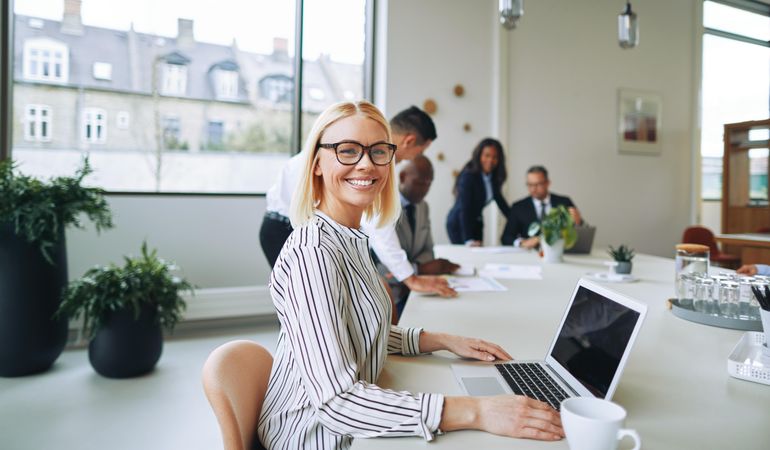 Woman looking up from her laptop and smiling in a bright office