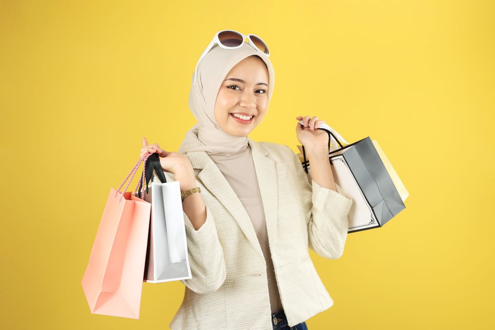 Smiling Feminine Young Muslimah Carrying Paper Shopping Bag on Yellow Background
