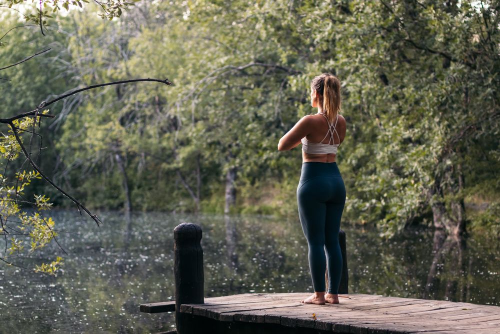 Woman in sportswear doing yoga outdoors near a lake