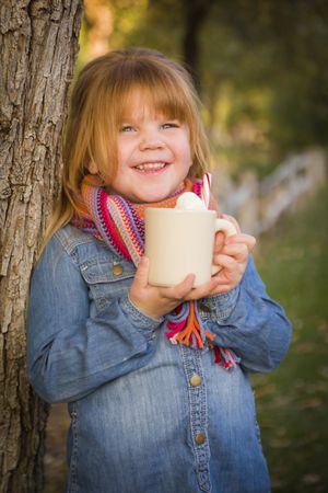 Cute Young Girl Holding Cocoa Mug with Marsh Mallows Outside