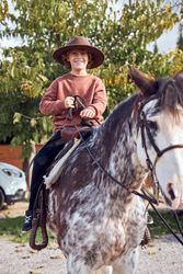 Boy in hat riding his brown mottled horse