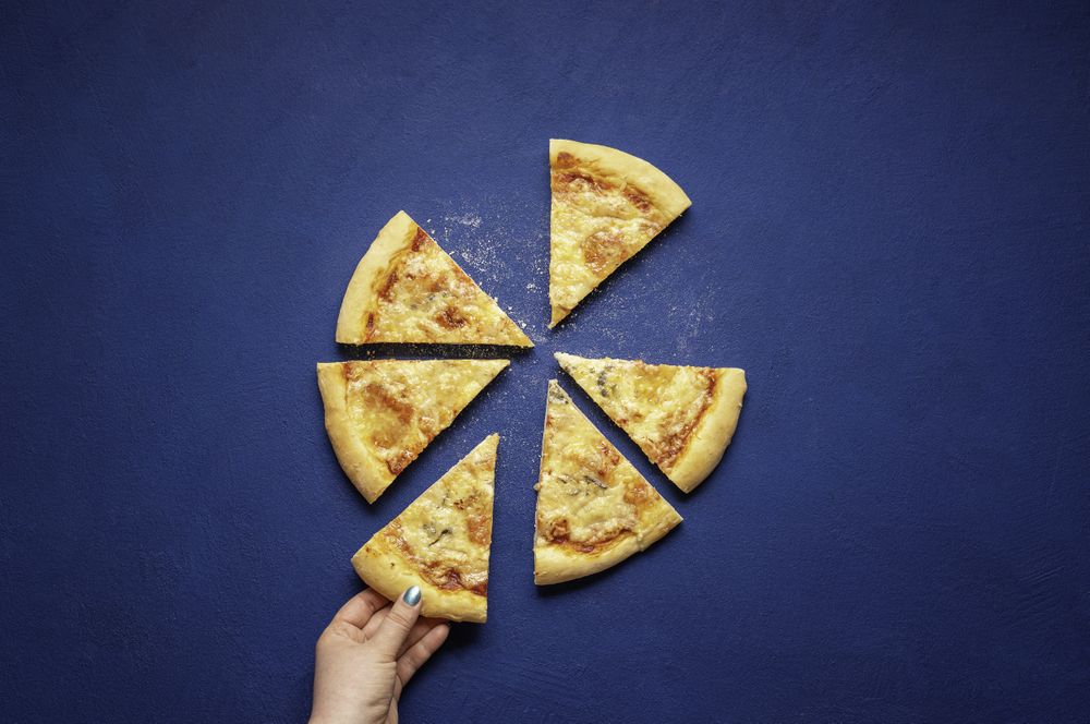 Someone taking a slice of four cheese pizza