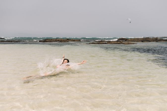 Woman in swimsuit lying in water on seashore