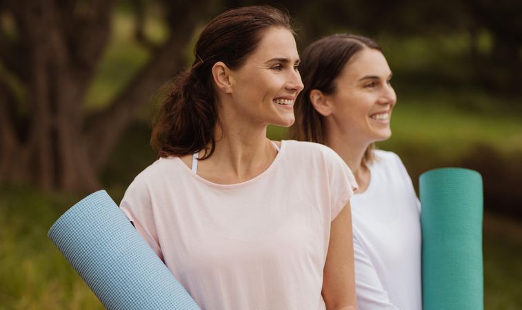 Close up of two smiling women standing in park with fitness mats