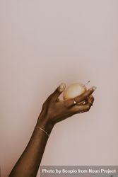 Black hand holding a pear wearing a gold bracelet against pastel pink background 4MwXG0