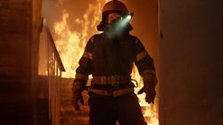 Firefighter with flashlight on helmet standing alone in burning staircase