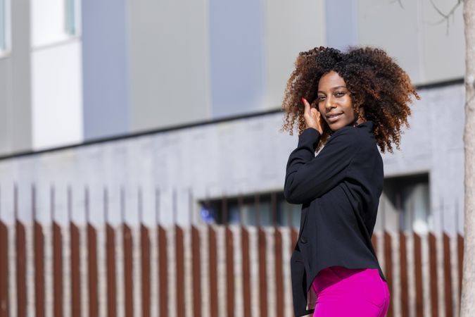 Black female putting her hair behind her ear while standing outside in the sun