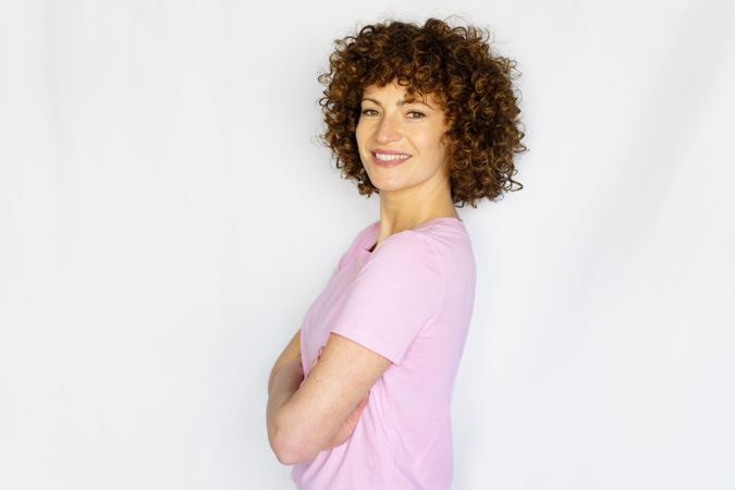 Smiling female in light pink t-shirt standing with arms crossed in blank space