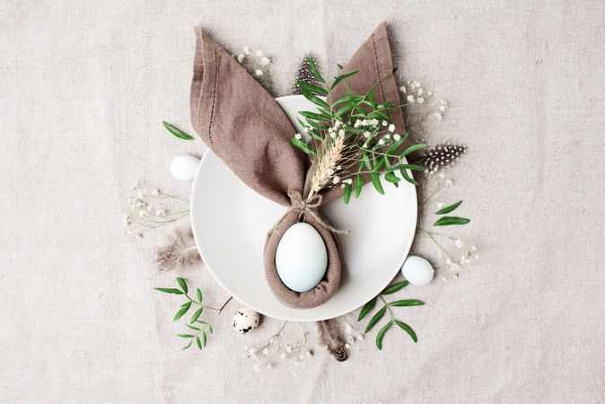 Napkin in rabbit ear shape on plate with egg in center surrounded by foliage