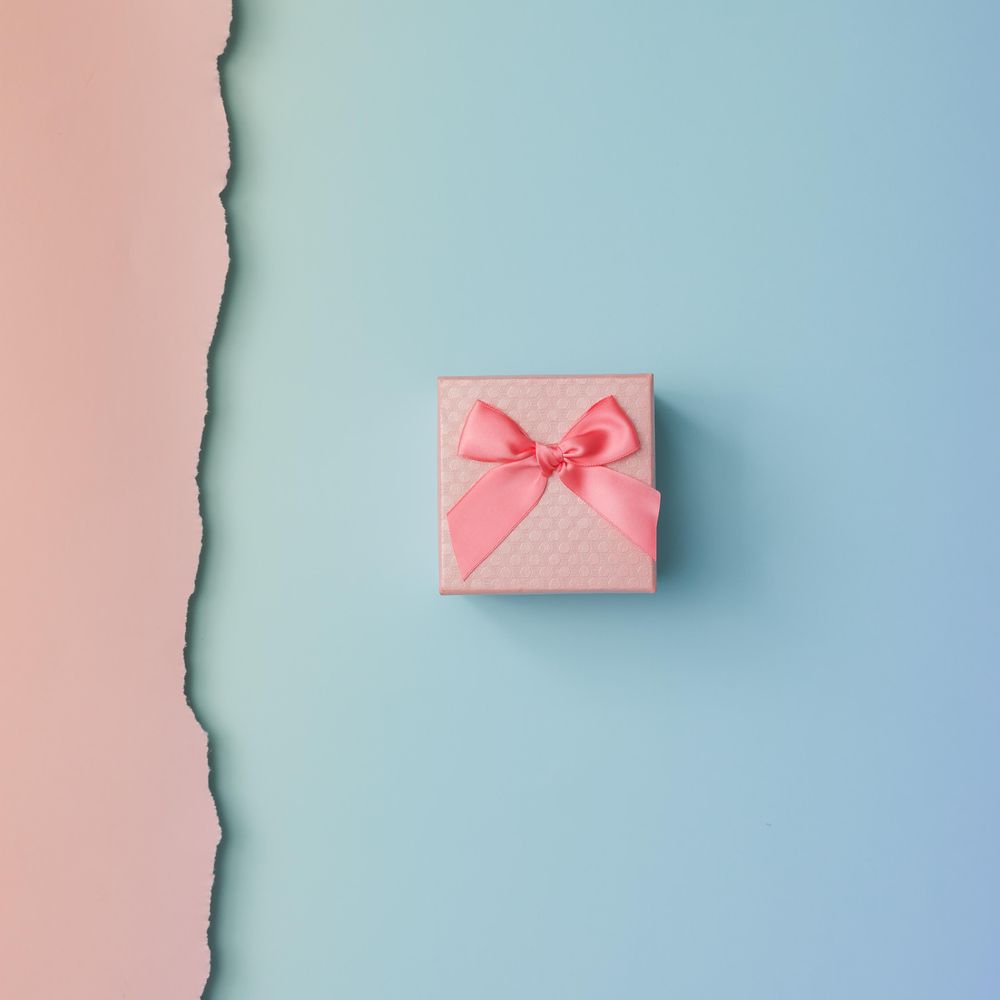 Close up shot of small gift wrapped with pink ribbon on pink blue background