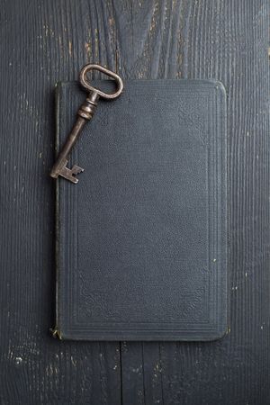 Vintage Key over dark leather book cover and wooden table