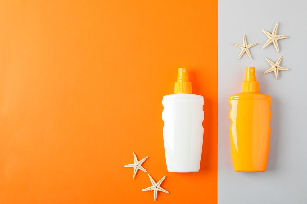 Flat lay composition with sunscreen sprays and starfishes on two tone background, space for text. Summer vacation backdrop