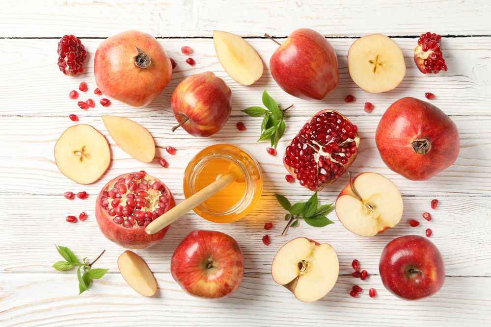 Looking down at fall fruit of pomegranates and apples with pot of honey on wooden table