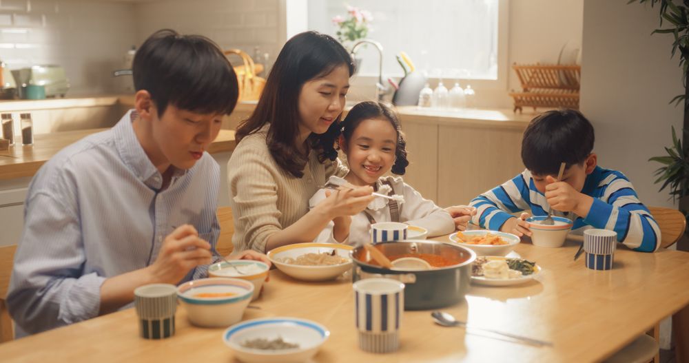 Happy Korean Family of Four Enjoying a Delicious Meal Together in Their Kitchen at Home.