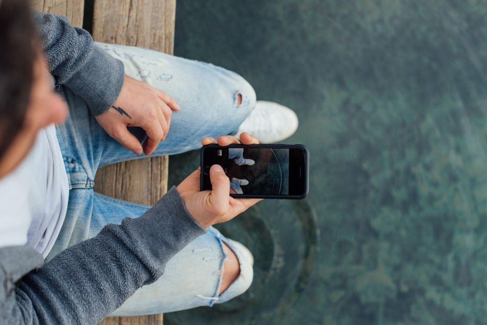 Man sitting on pier over water with smart phone