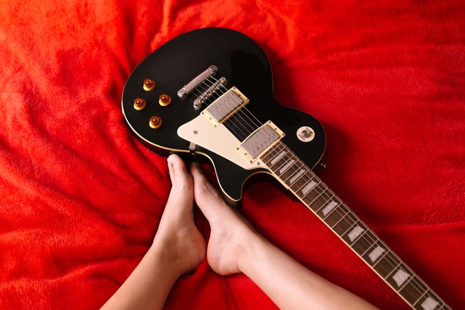Crop female musician with electric guitar on bed