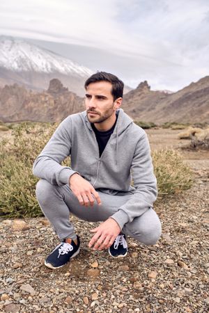 Confident young man squatting on stony ground in cloudy day