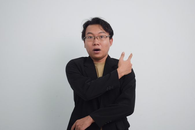 Surprised Asian businessman with suit and casual shirt pointing behind