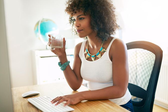 Black female sipping drink as she works at her computer