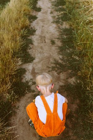 Anonymous kid sitting on haunches on pathway in countryside