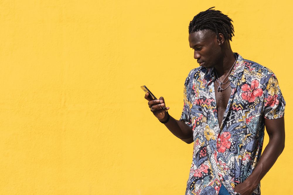 Stylish Black man in colorful shirt with smartphone