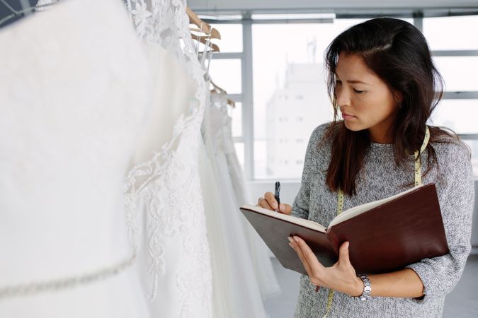 Female dressmaker working in bridal wear and writing in a diary