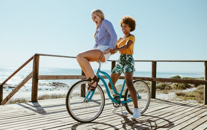 Young woman balancing on the handlebars of a bicycle ridden by her friend on a summer day