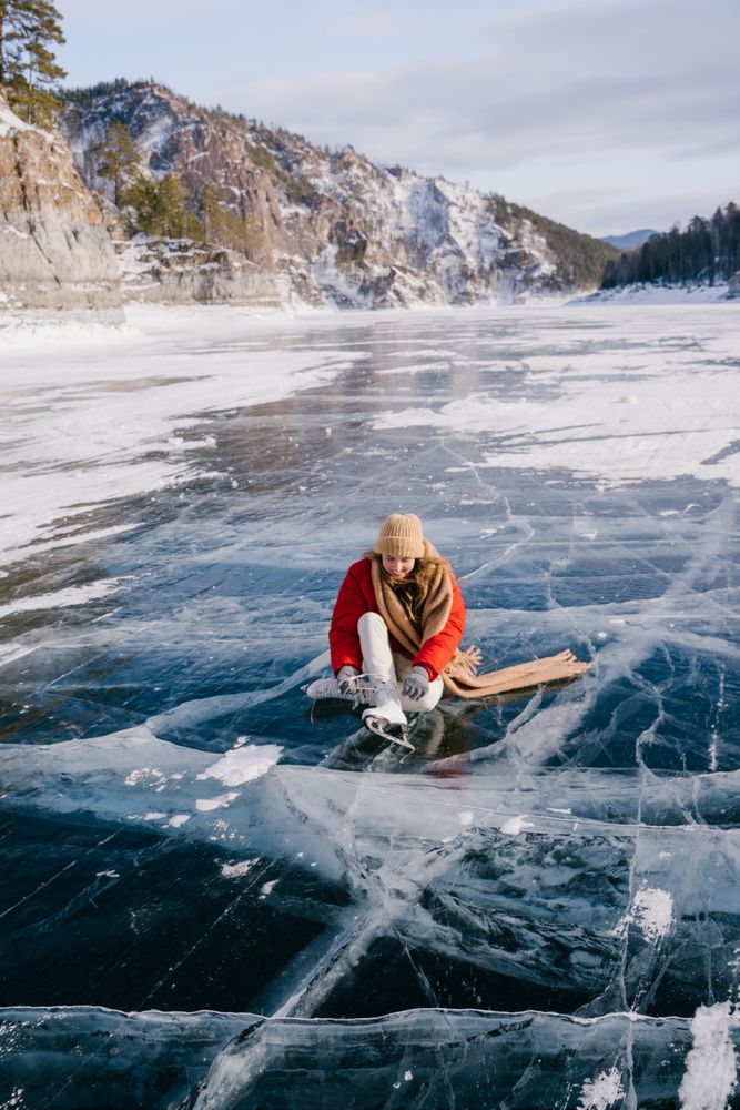 Woman sitting on frozen river and tying the shoelaces