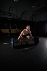 Young strong sportsman doing exercises with barbell with weights