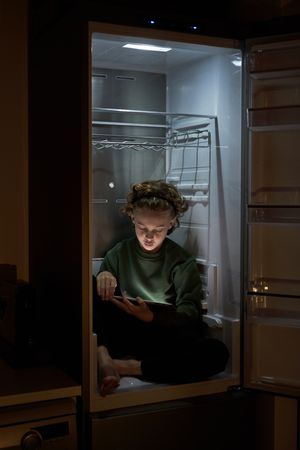 Boy sitting in fridge with tablet