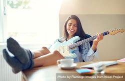 Woman having fun and smiling while playing guitar at her desk 4jLkW0
