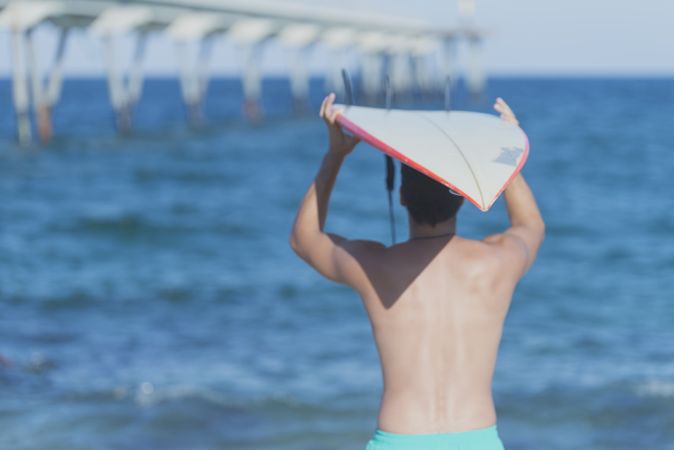 Mid body shot of male surfer looking out to the ocean with board on head