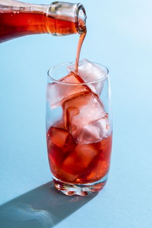 Pouring strawberry syrup over ice in a glass
