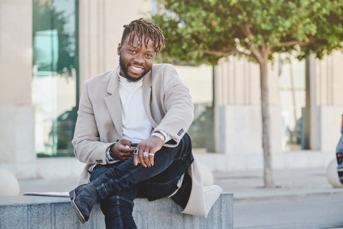 Cheerful Black man browsing cellphone while sitting on street