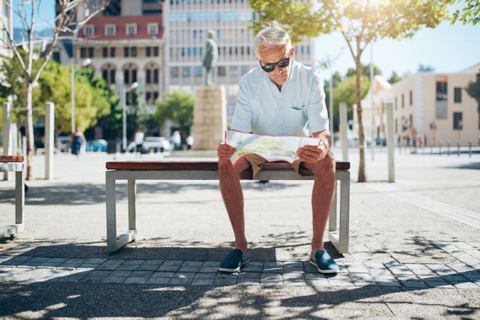 Male tourist sitting on a bench outside and looking at a map