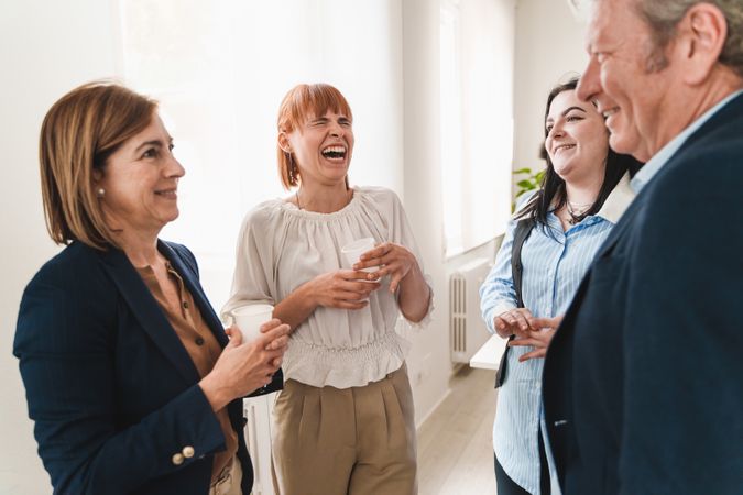Colleagues taking a break in office, standing near a window and sharing a laugh
