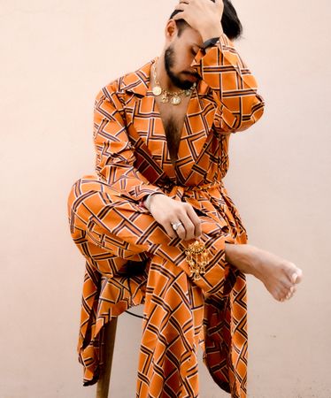 Man in orange plaid outfit sitting on chair against pink wall