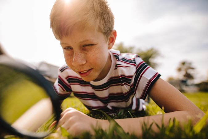Boy looking through magnifying glass in the grass on a sunny day