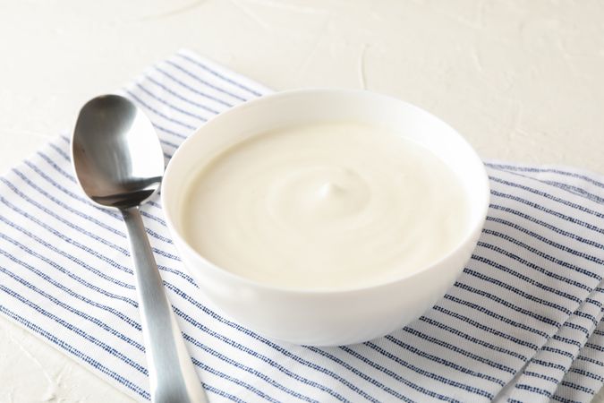 Bowl of sour cream yogurt, spoon and towel on cement background