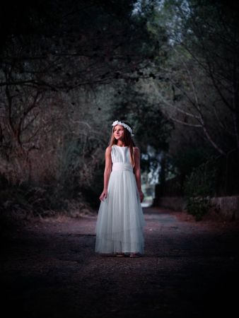 Elegant girl in white dress standing on dark path with closed gr