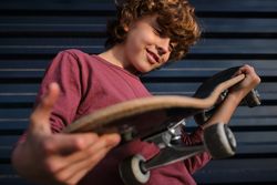 Glad boy examining skateboard near wall