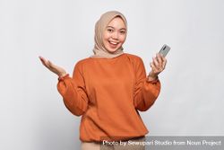 Muslim woman smiling with open gesture and holding smartphone 5Xv1Qb