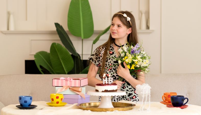 Girl posing with flowers and birthday cake with presents