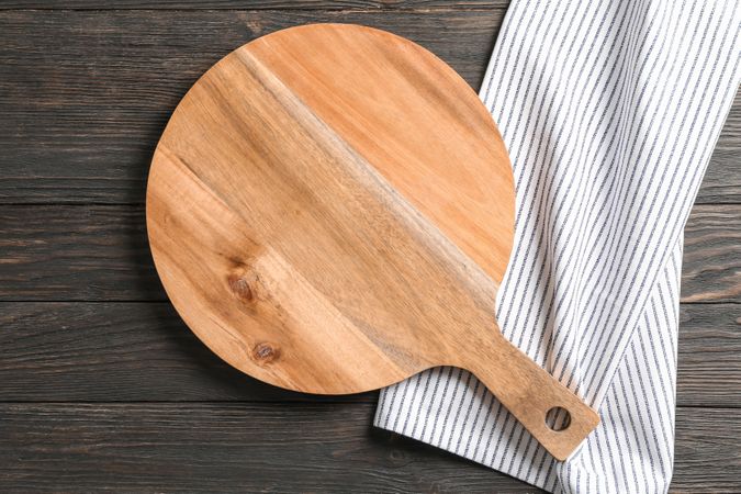 Cutting board with kitchen towel on wooden background, space for text
