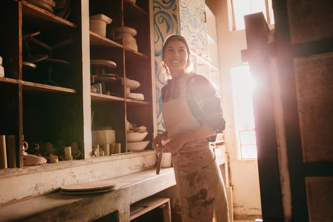 Female potter in sunny pottery workshop adjusting her apron