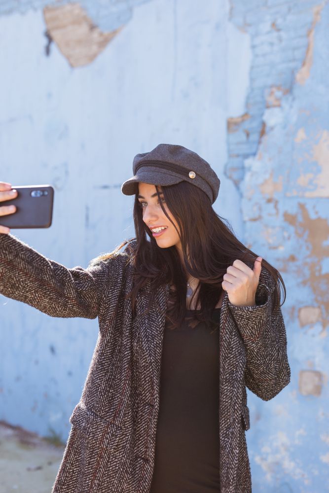 Charming Hispanic woman taking selfie near wall