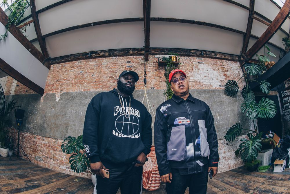 Fisheye wide angle up shot of two Black men standing against industrial exposed brick wall