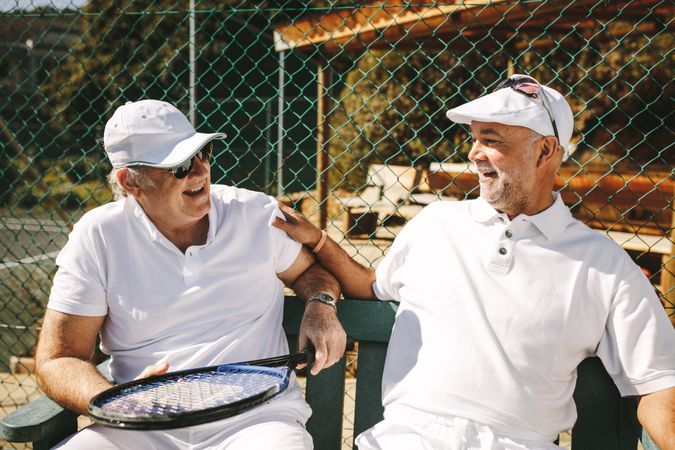 Mature men talking to each other sitting on bench during a game of tennis