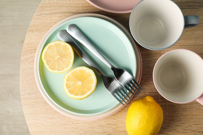 Plates and cups with lemons on wooden table, top view