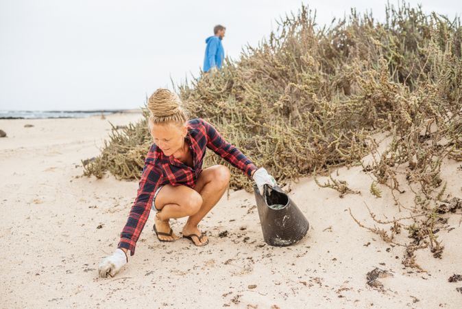Content modern woman picking litter from sandy seashore